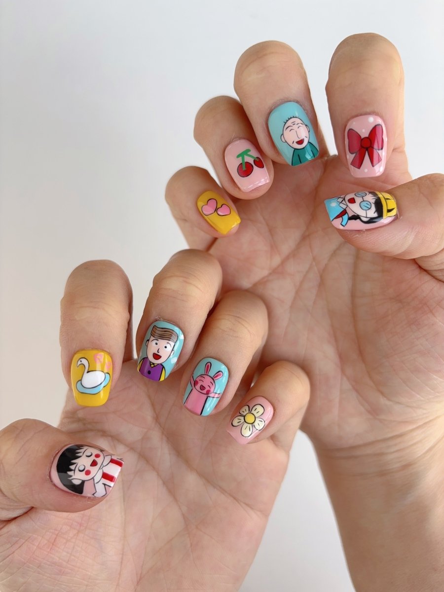 Ten-piece handmade press-on nail set with mixed art: pink swan, yellow hearts, cherry fruit, smiling faces, and cute patterns