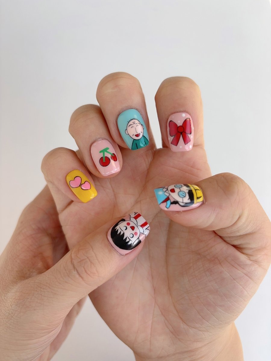 Close-up of short square press-on nails with colorful anime-inspired designs including a bow, bunny, daisy, and cartoon girl