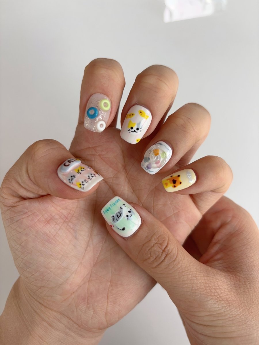 Close-up of 3D cat and candy press-on nails featuring sculpted butterfly, glitter bubbles, and yellow fish accents