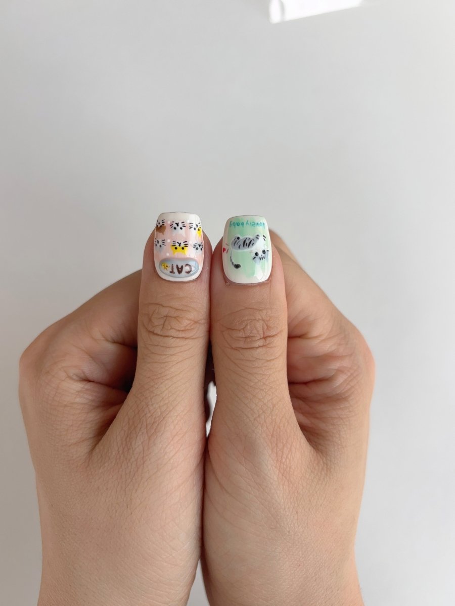 Thumbs showing detailed 3D press-on nails with cat art and bubble-like embellishments on a clean white base