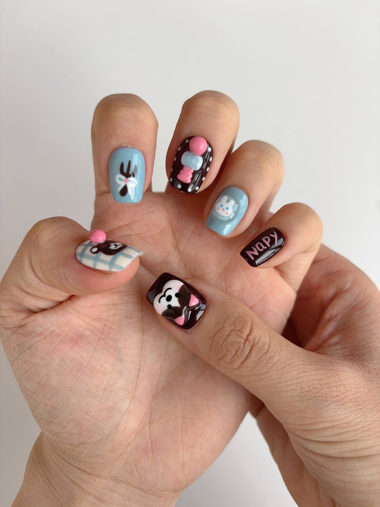 Close-up of kawaii animal press-on nails with bubblegum bear, pink text, and sculpted bunny head on short square nails