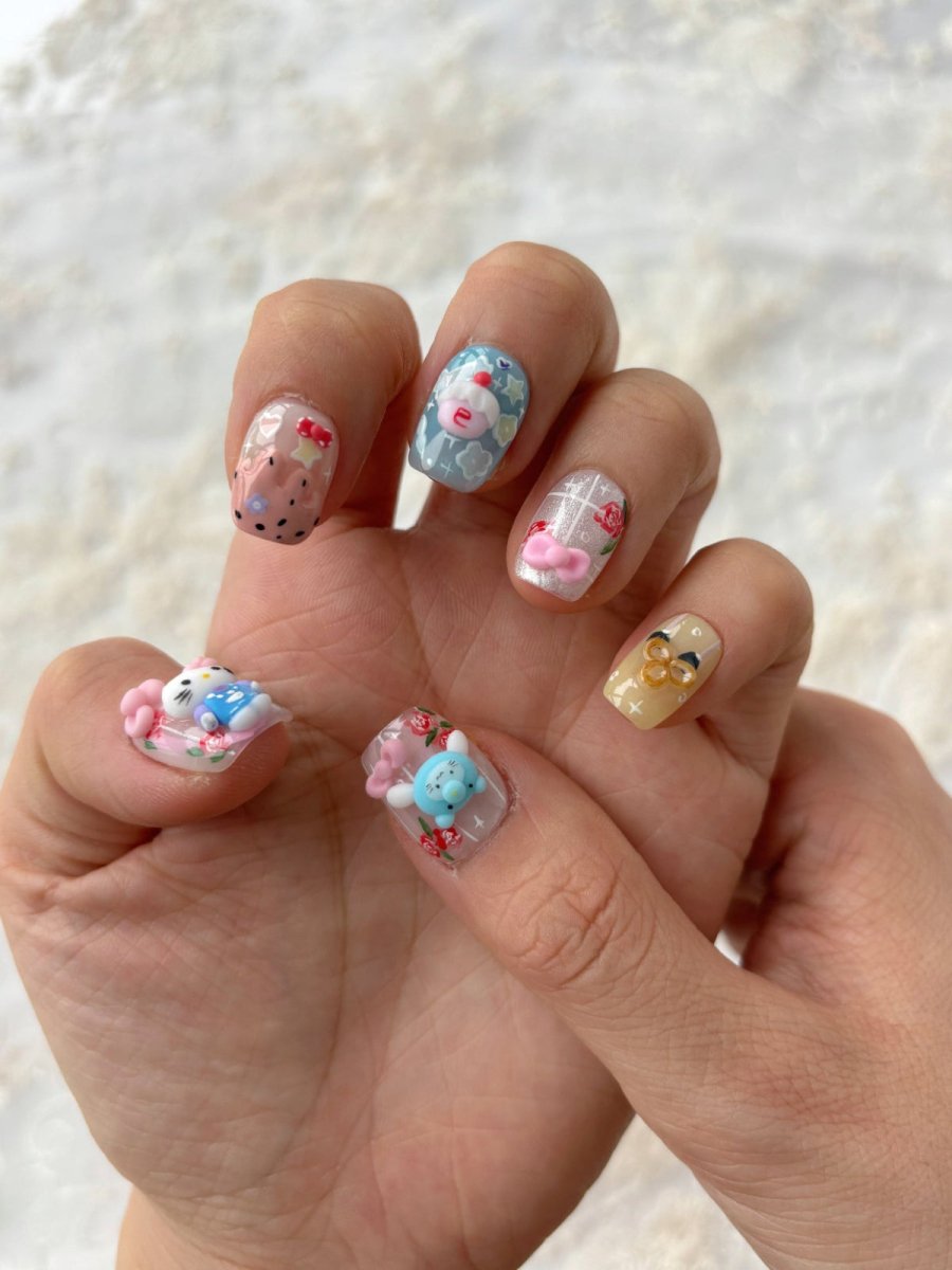 Hand wearing Hello Cutie Carnival press-on nails featuring 3D Hello Kitty, blue bear, cupcake, and bow details