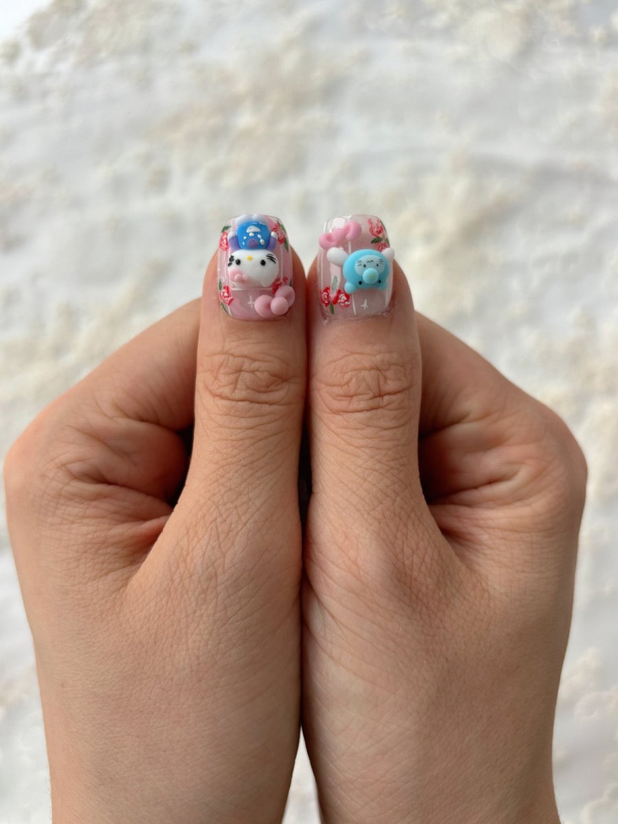 Close-up of both thumbs showing Hello Kitty and blue bear press-on nails with floral designs and sculpted charms