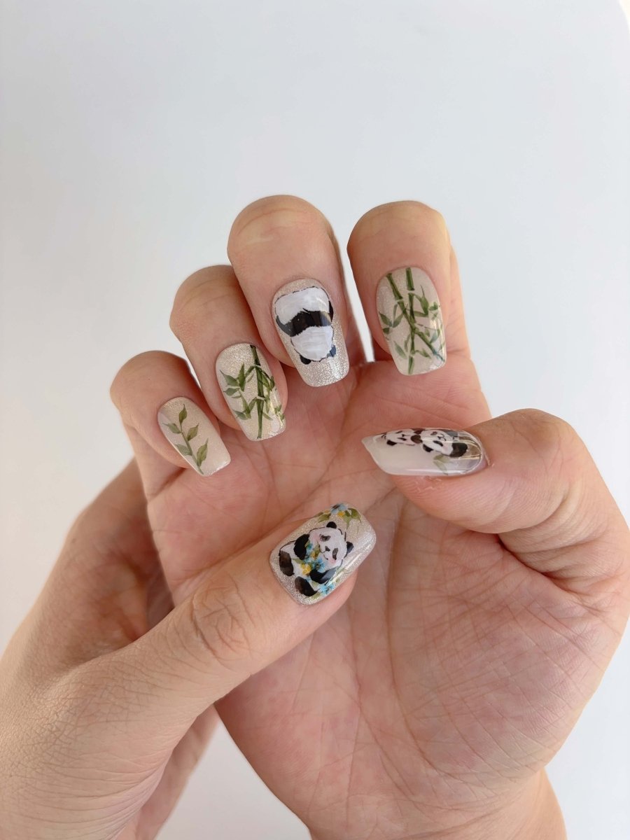 Close-up of panda nail art featuring daisies and greenery on shimmer nude base