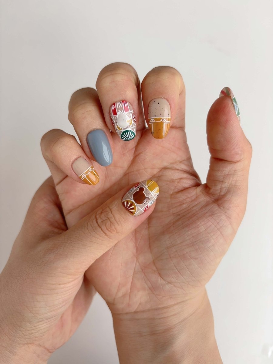 Short oval nails with mustard, sage, and red stained-glass patterns with hand-drawn forest creatures