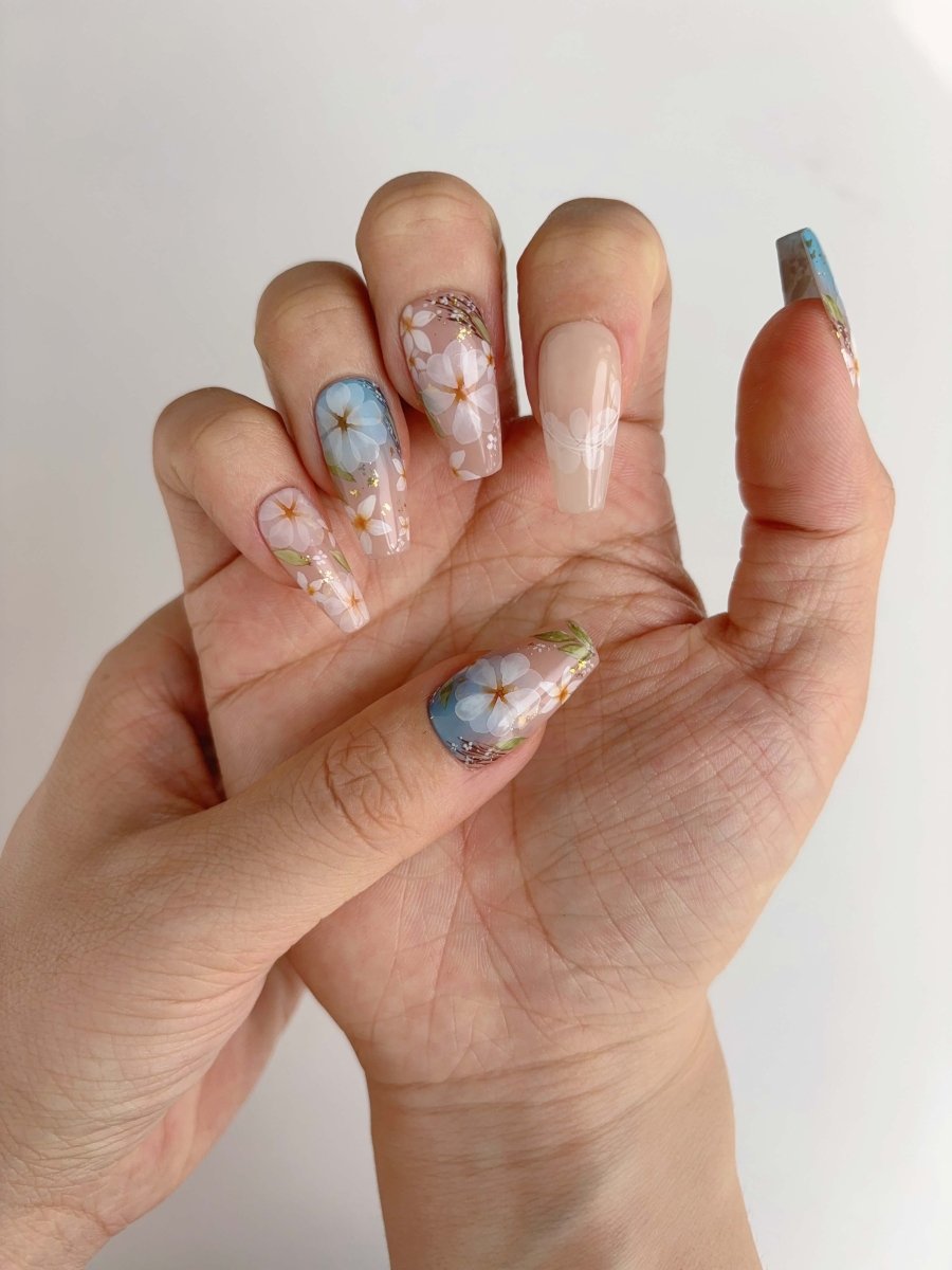 Close-up of daisy nail art featuring white petals and yellow centers over sky-inspired gradient