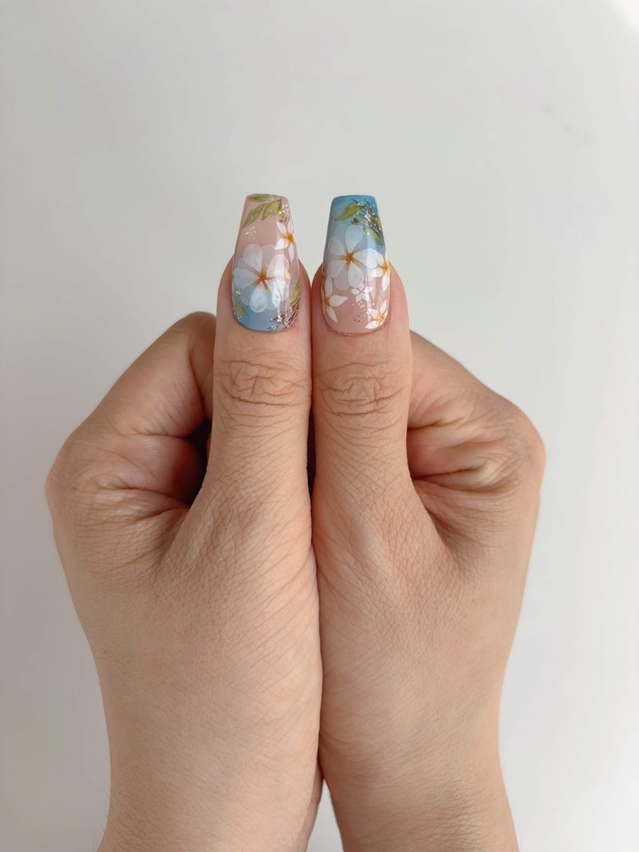 Thumb-to-thumb view showing hand-painted daisies and clear nude tips with shimmer finish