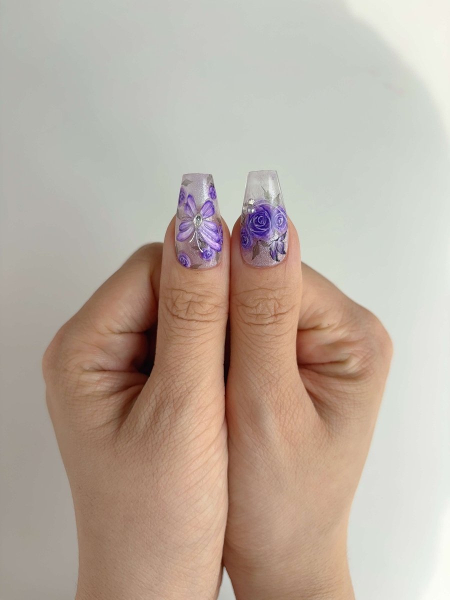 Thumb close-up of lavender rose and 3D butterfly press-on nails with rhinestone accents