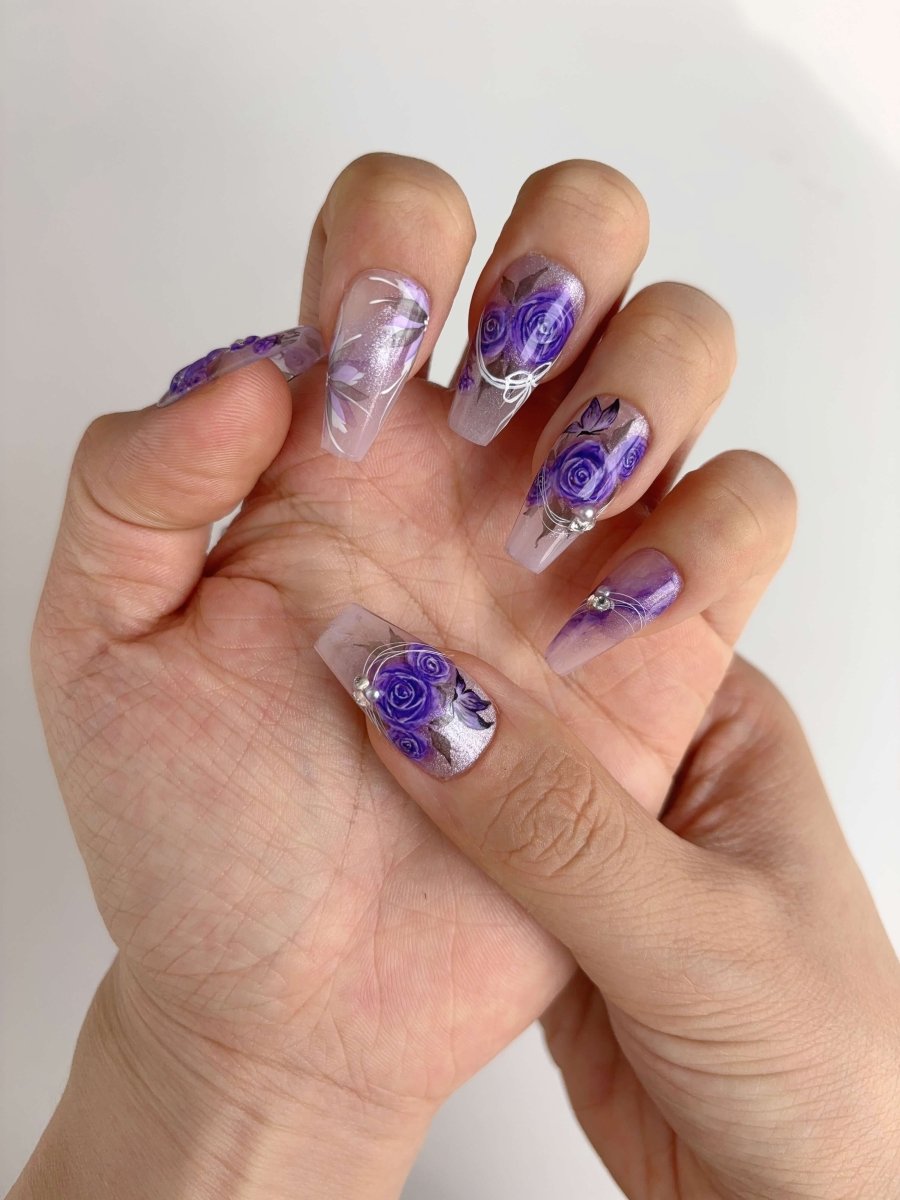 Hand wearing floral press-on nails with purple rose artwork and shimmer finish