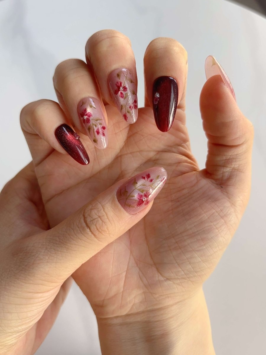 Close-up of hand wearing Crimson Bloom nails with floral and foil detail