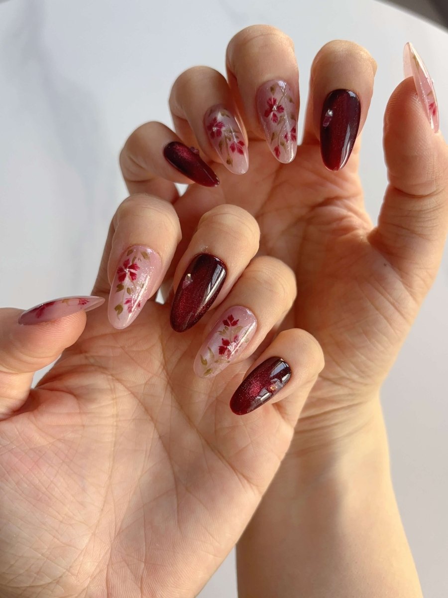 Hand display of Crimson Bloom press-ons showing wildflower overlays and reflective finish