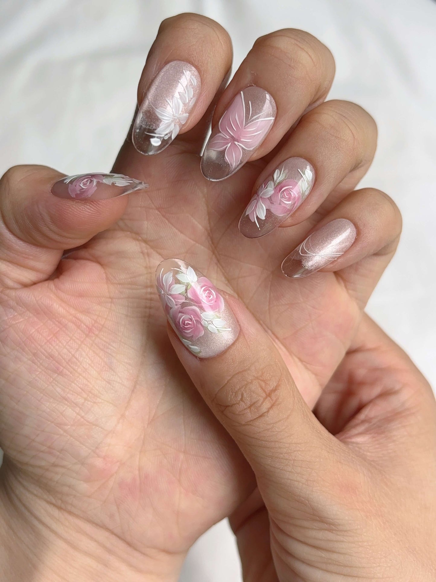 Close-up hand wearing Rosé Reverie press-on nails with white floral accents