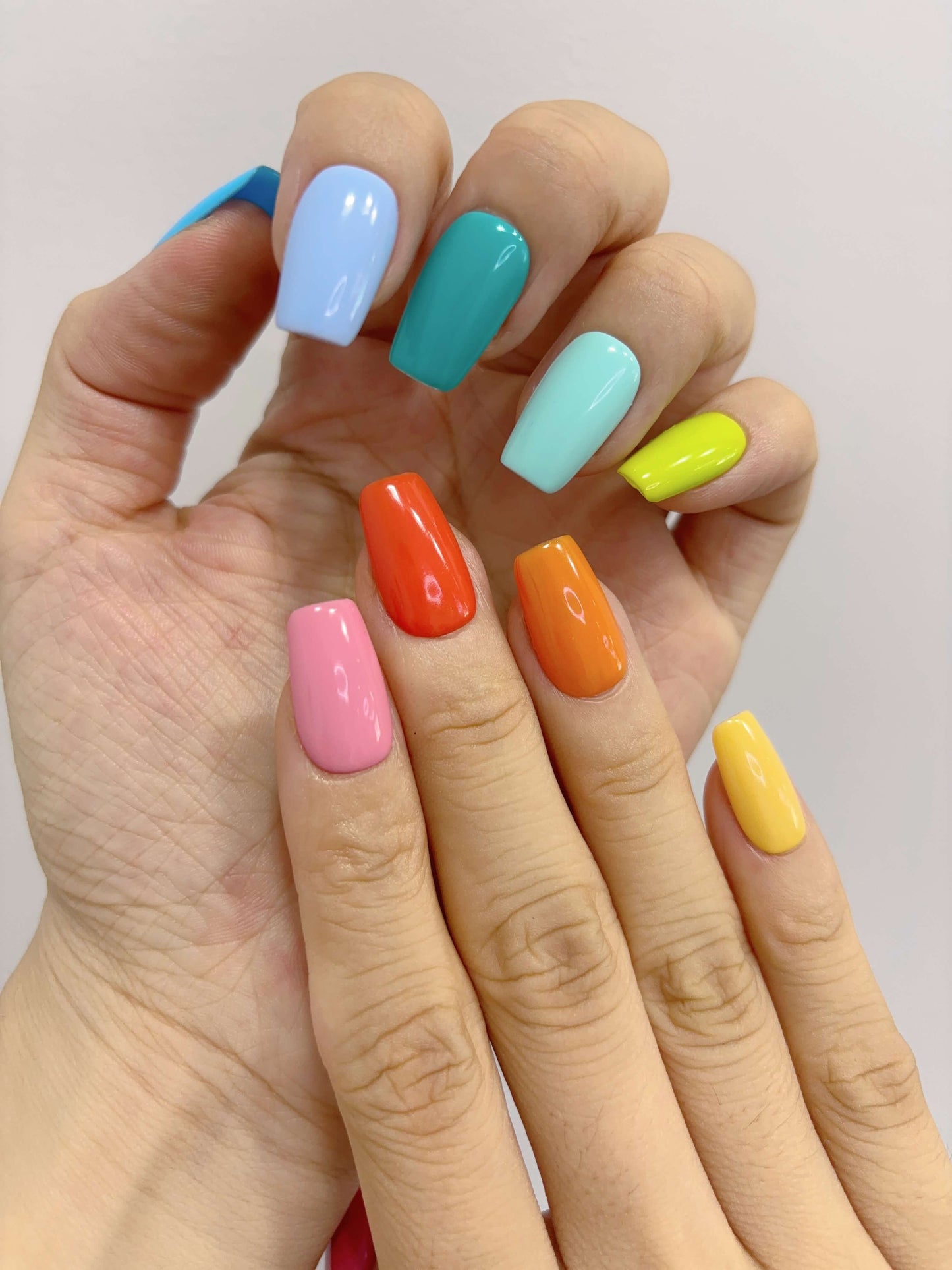 Overlapping hands showcasing full rainbow colour nail spread