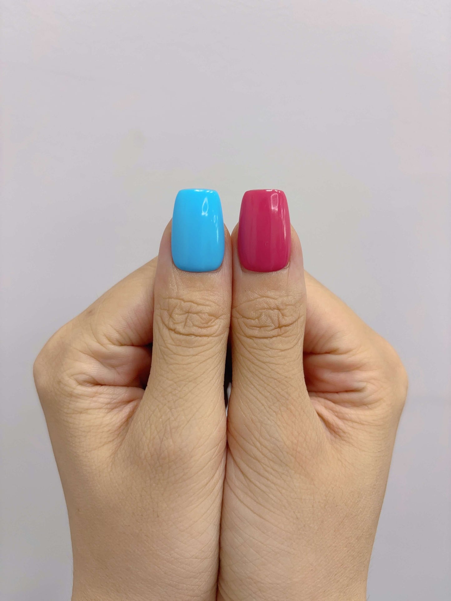 Close-up of thumbs featuring bold red and sky blue polish from Technicolor Tips