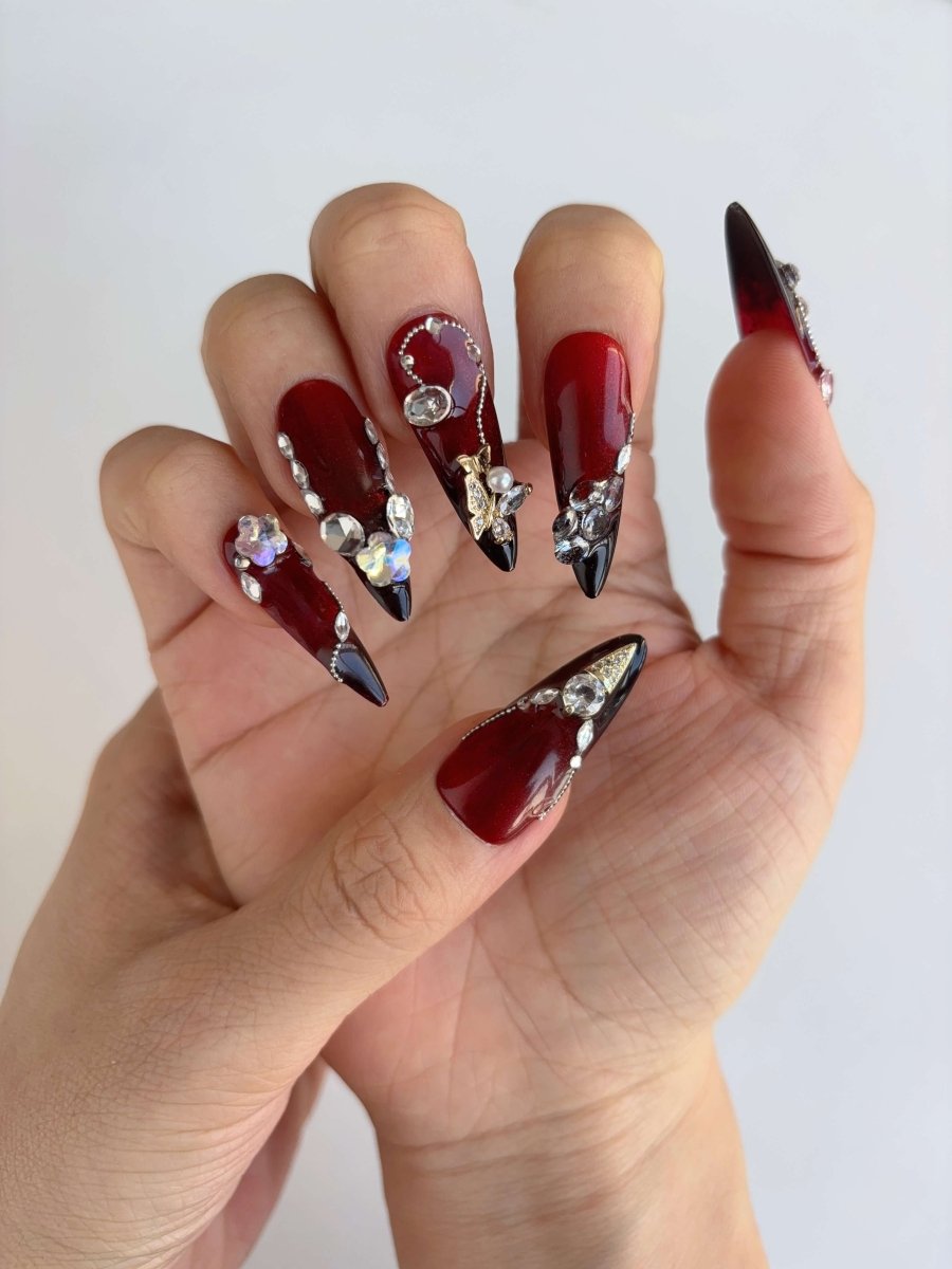 Hand pose with deep red and black ombré nails covered in crystals and rhinestones