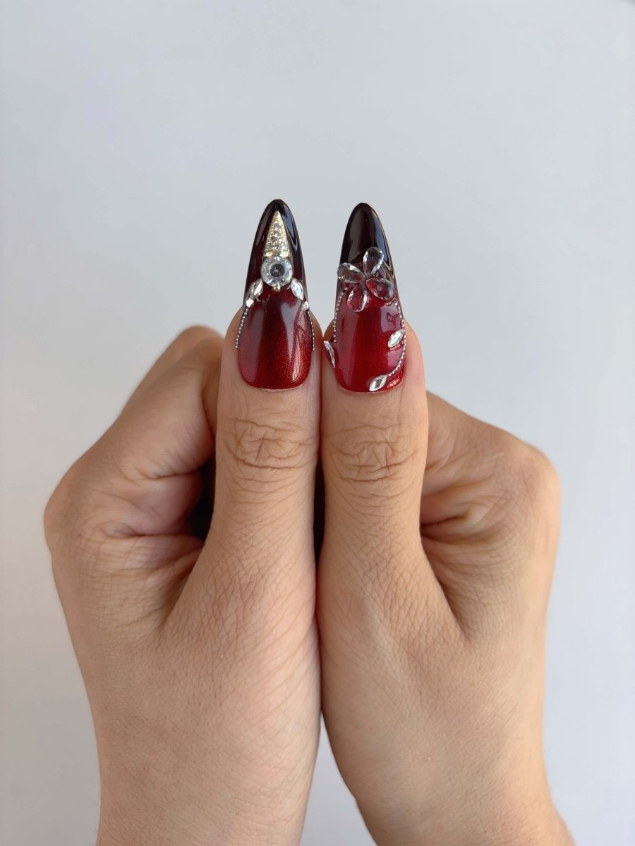 Thumbs featuring crystal-detailed long stiletto nails with silver and black accents