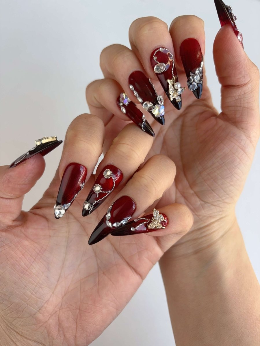 Both hands showcasing dramatic red stiletto nails with chain and gem details