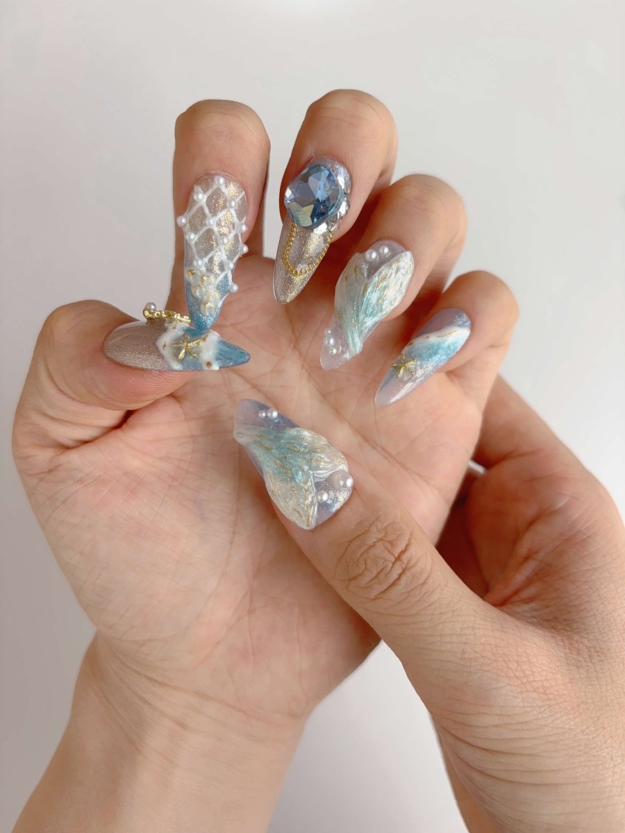 Close-up of hand wearing 3D ocean-themed press-on nails with net texture and blue gem accents