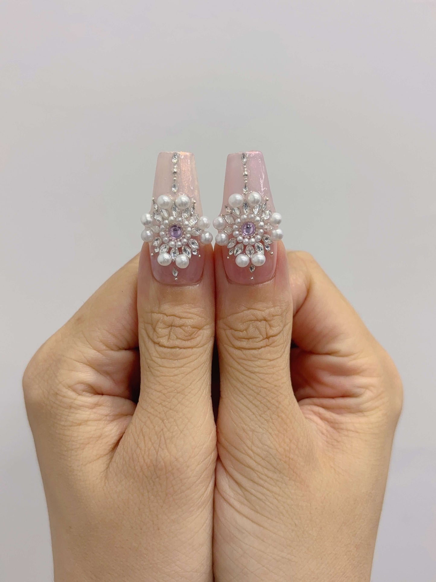 Close-up of thumbs wearing Pearl Eclipse nails with statement pearl centerpiece