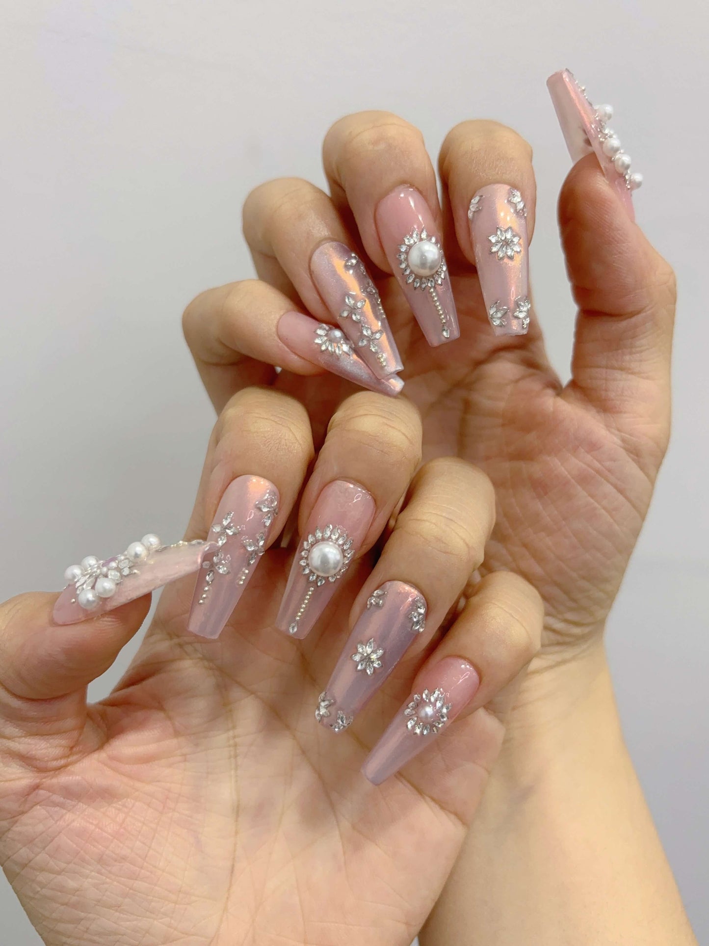 “Two hands showing full Pearl Eclipse nail set with iridescent base and crystal embellishments