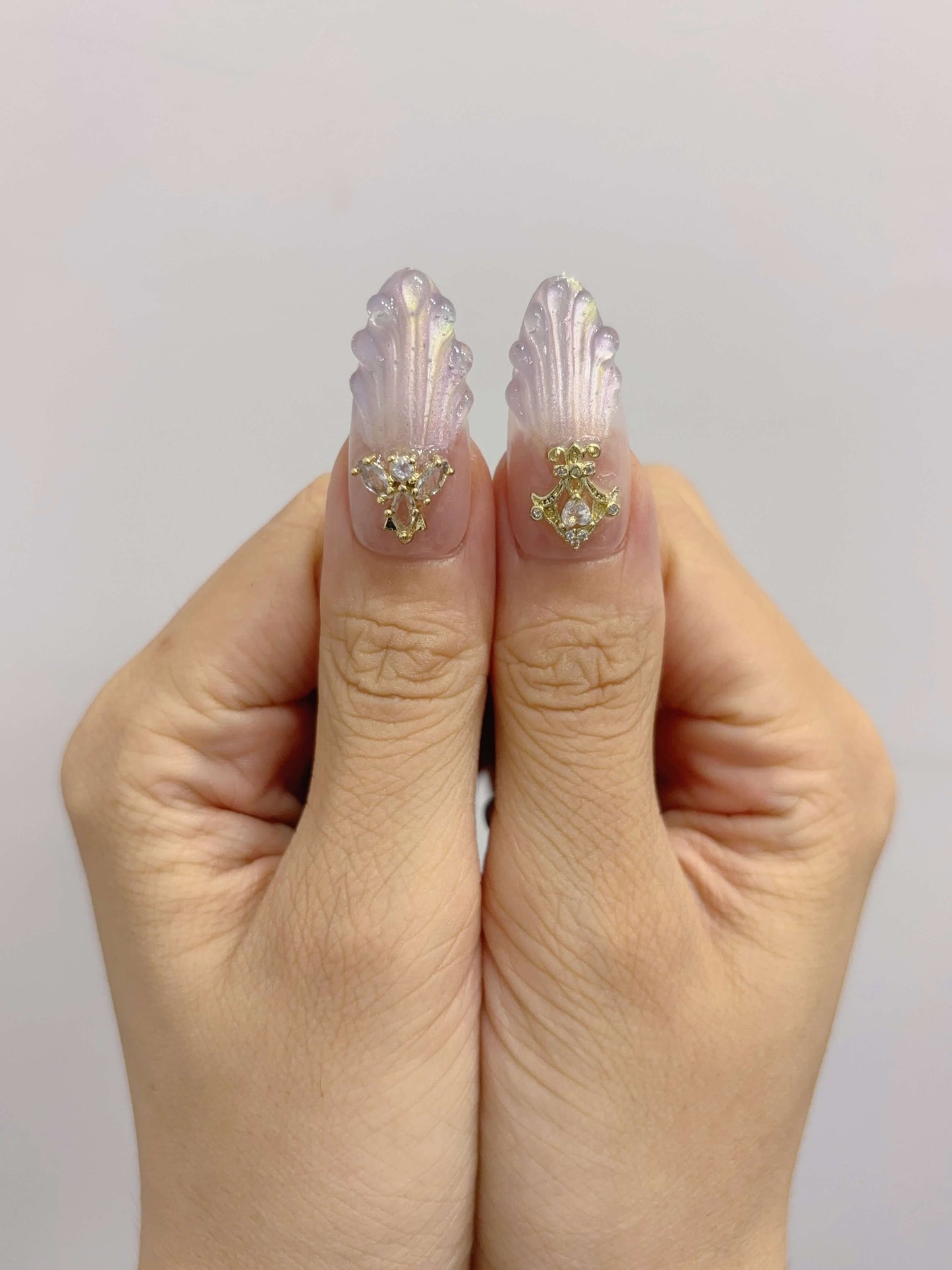 Close-up of thumbs with crown and bow charms on sculpted shell background