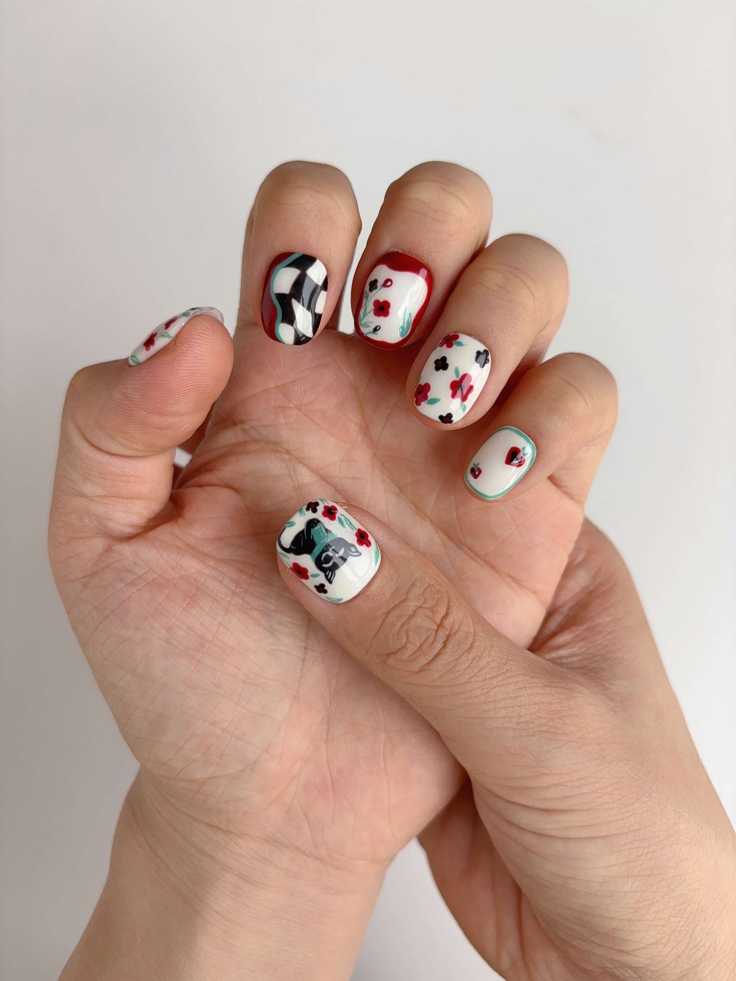 Hand wearing Lucky Cat Bloom nails with kawaii black cat and red flower accents