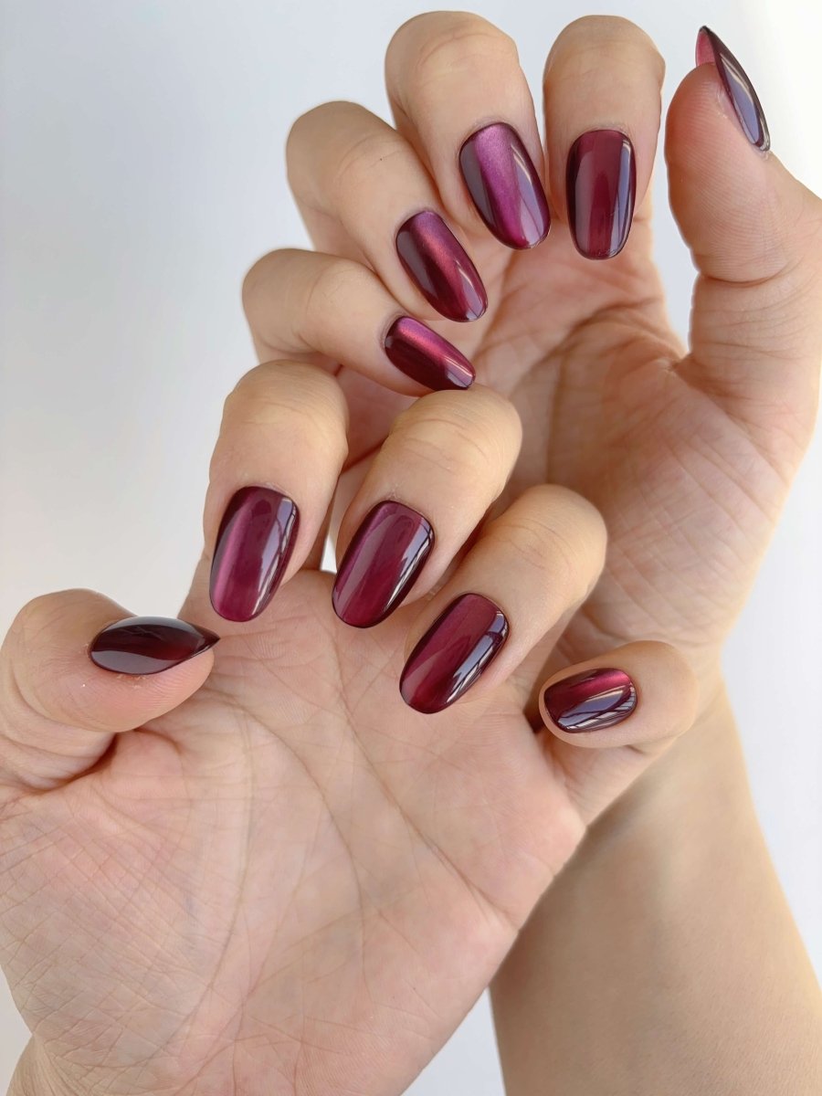 Hand with short burgundy cat's eye nails shown from above