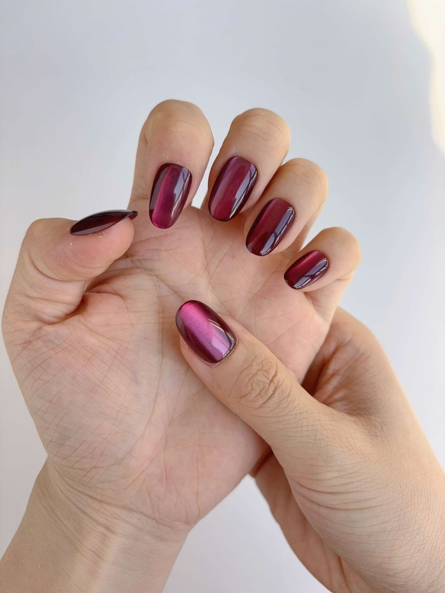 Close-up of burgundy magnetic shimmer press-on nails worn on hands