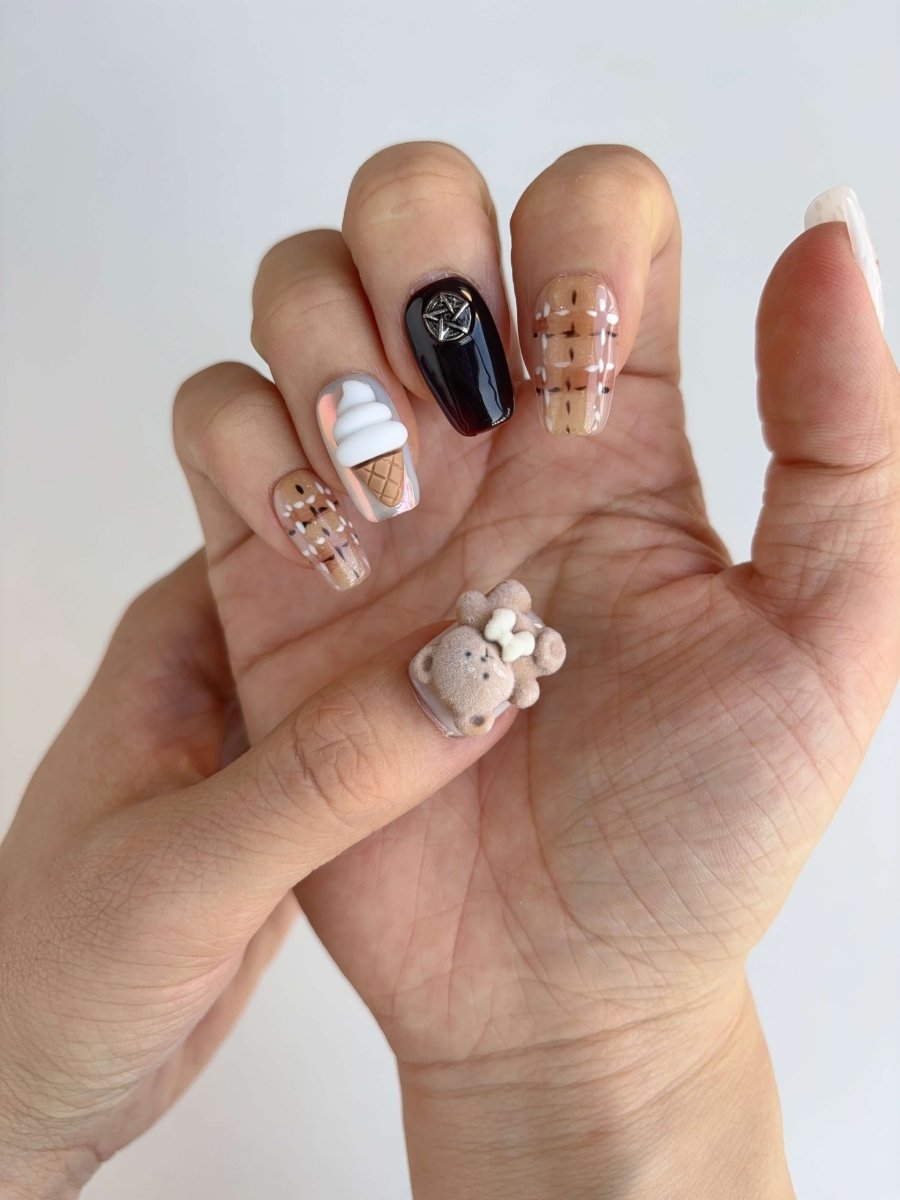 Full hand wearing kawaii press-on nails with teddy bear, ice cream cone, and plaid design