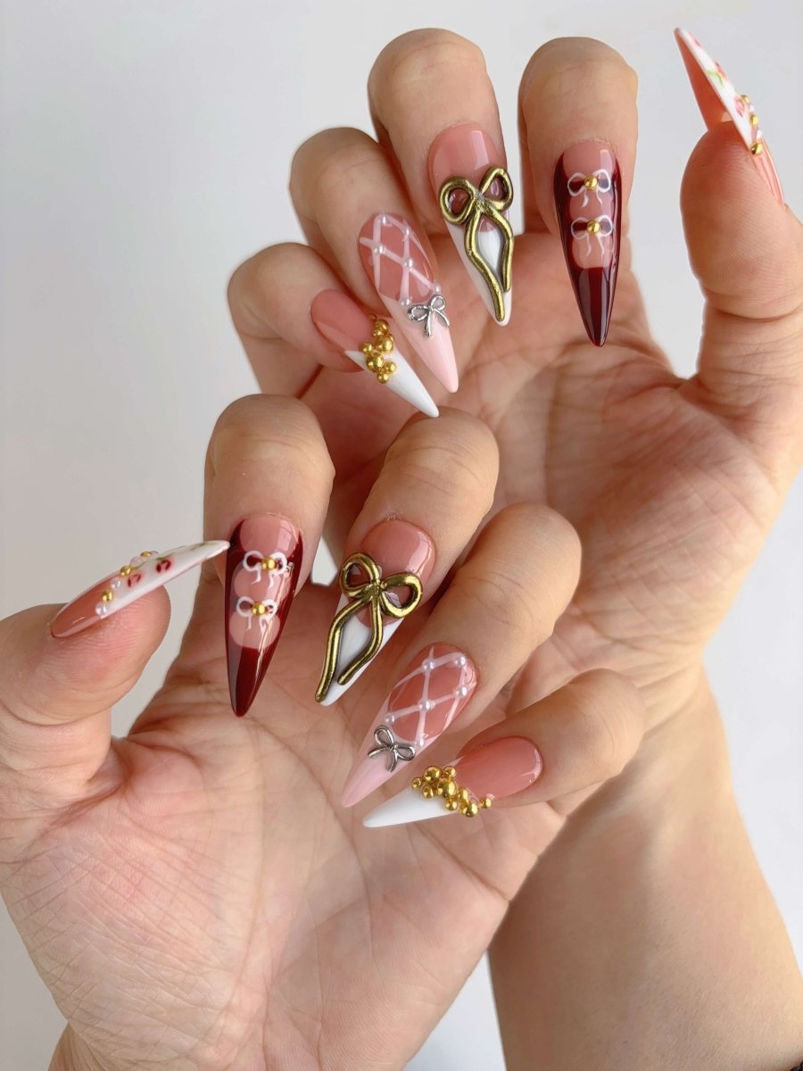 Two hands with glossy pink, red, and white stiletto nails featuring sculpted bows, pearl details, and quilted effects