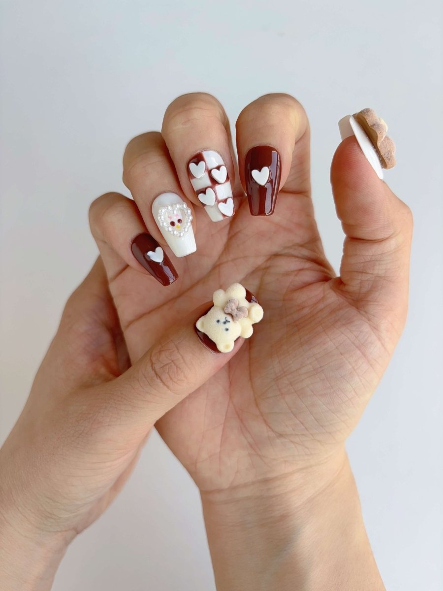 Hand wearing blush and cocoa press-ons with raised heart and red gem detail