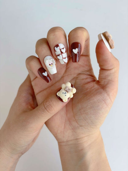Hand wearing blush and cocoa press-ons with raised heart and red gem detail