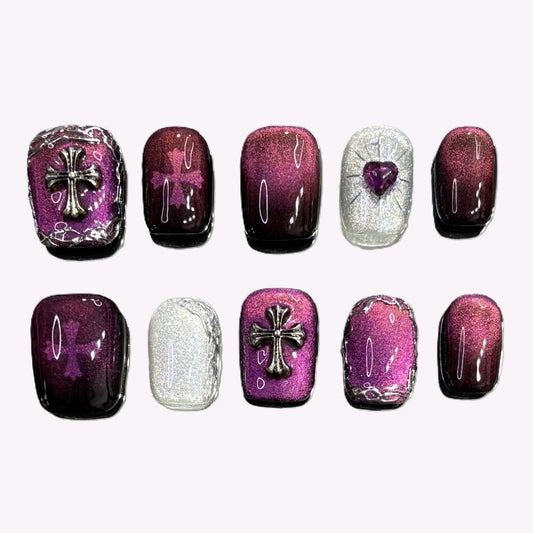 Flat lay of Garnet Eclipse press-on nails featuring cross charms, glitter, and heart gem