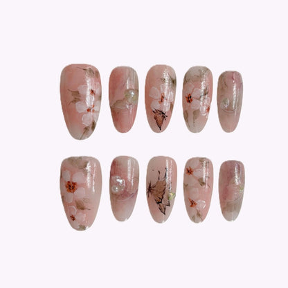 Close-up of Sakura Whisper press-on nails with blush pink base and cherry blossom design in storage case