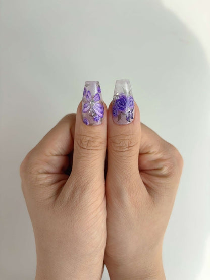 Thumb close-up of lavender rose and 3D butterfly press-on nails with rhinestone accents
