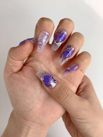 Hand wearing floral press-on nails with purple rose artwork and shimmer finish