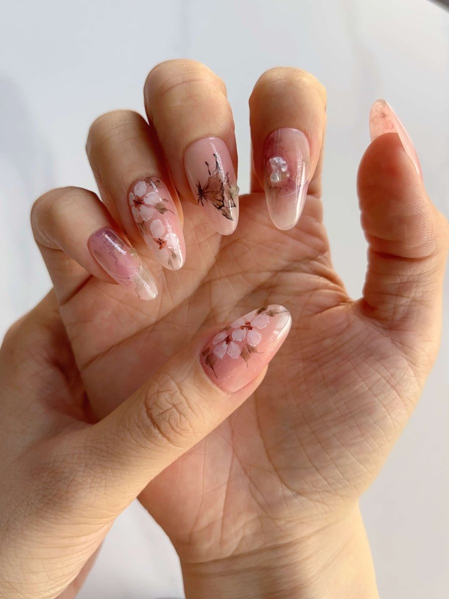 Hand model wearing Sakura Whisper press-ons showing butterfly and floral accents