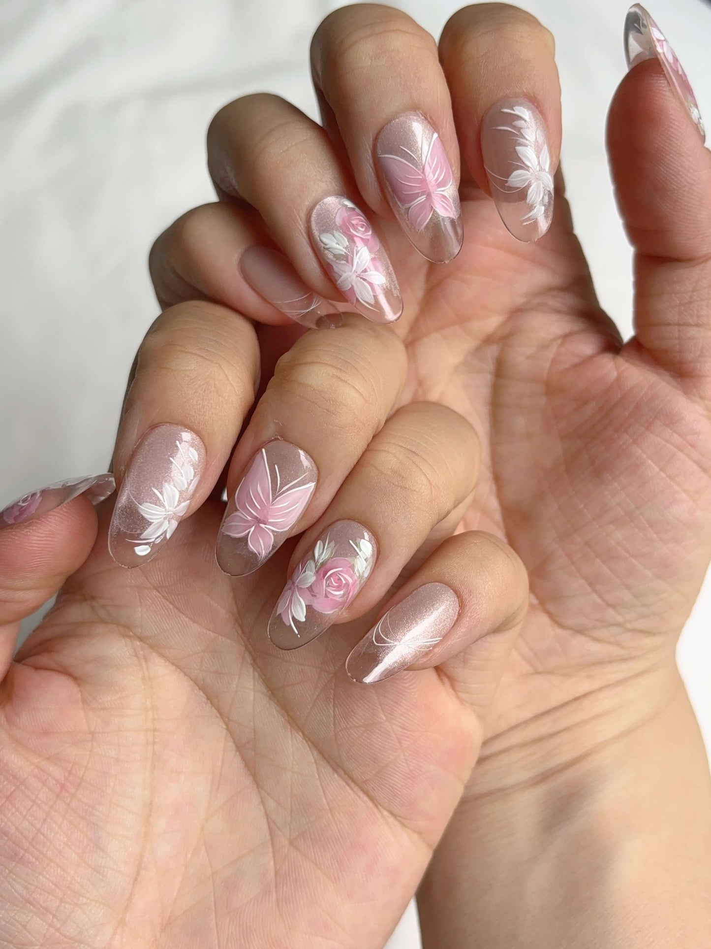 Two hands showing Rosé Reverie nails with soft floral and butterfly design