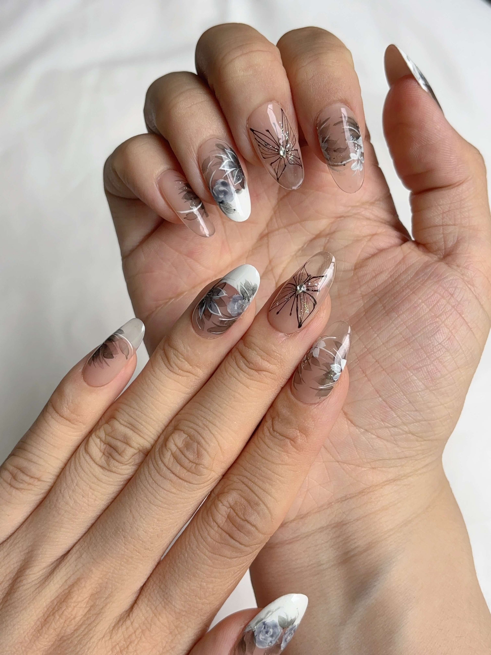 Close-up of hand wearing Twilight Garden press-on nails with butterfly detail