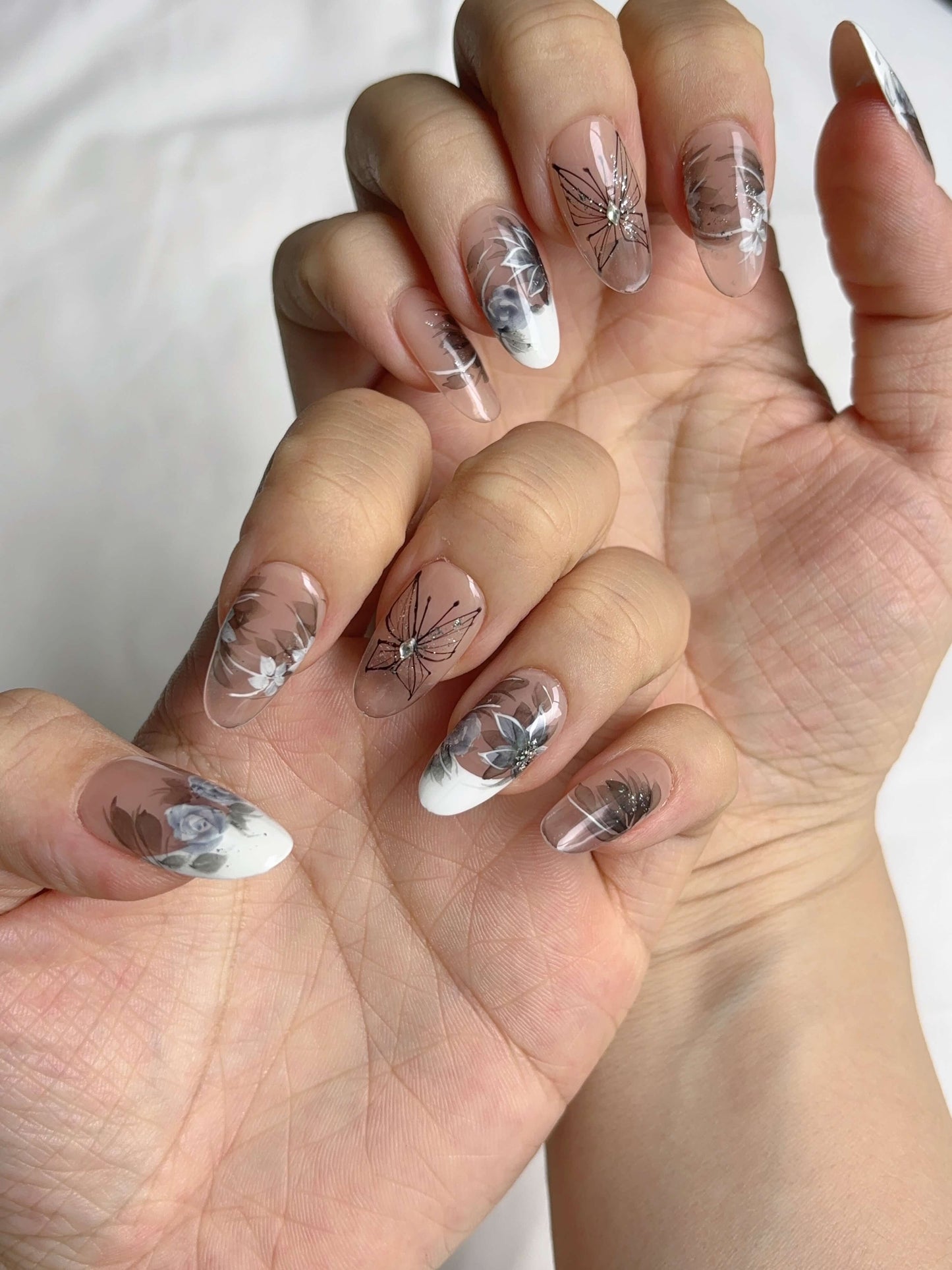 Two hands showing full Twilight Garden nail set in floral and grey-white hues