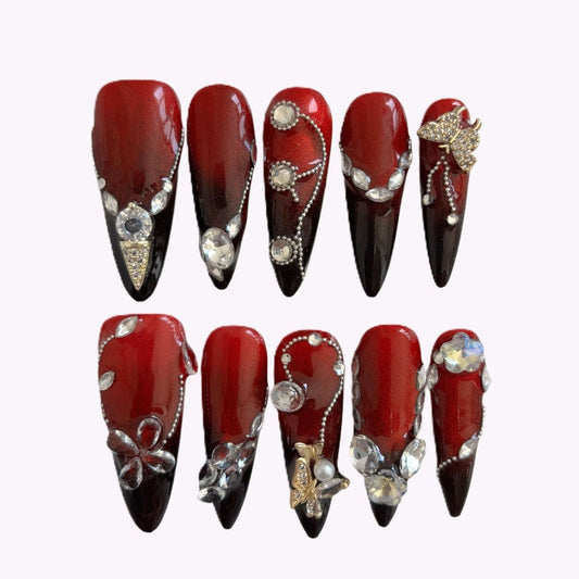 Full nail set in a case featuring red to black ombré stiletto nails with crystals and 3D embellishments