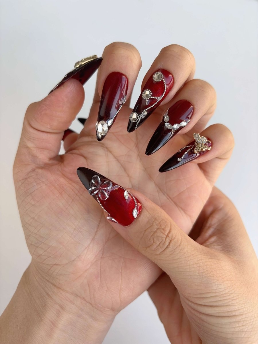 Close-up of long stiletto press-on nails in red and black ombré with rhinestone and butterfly accents