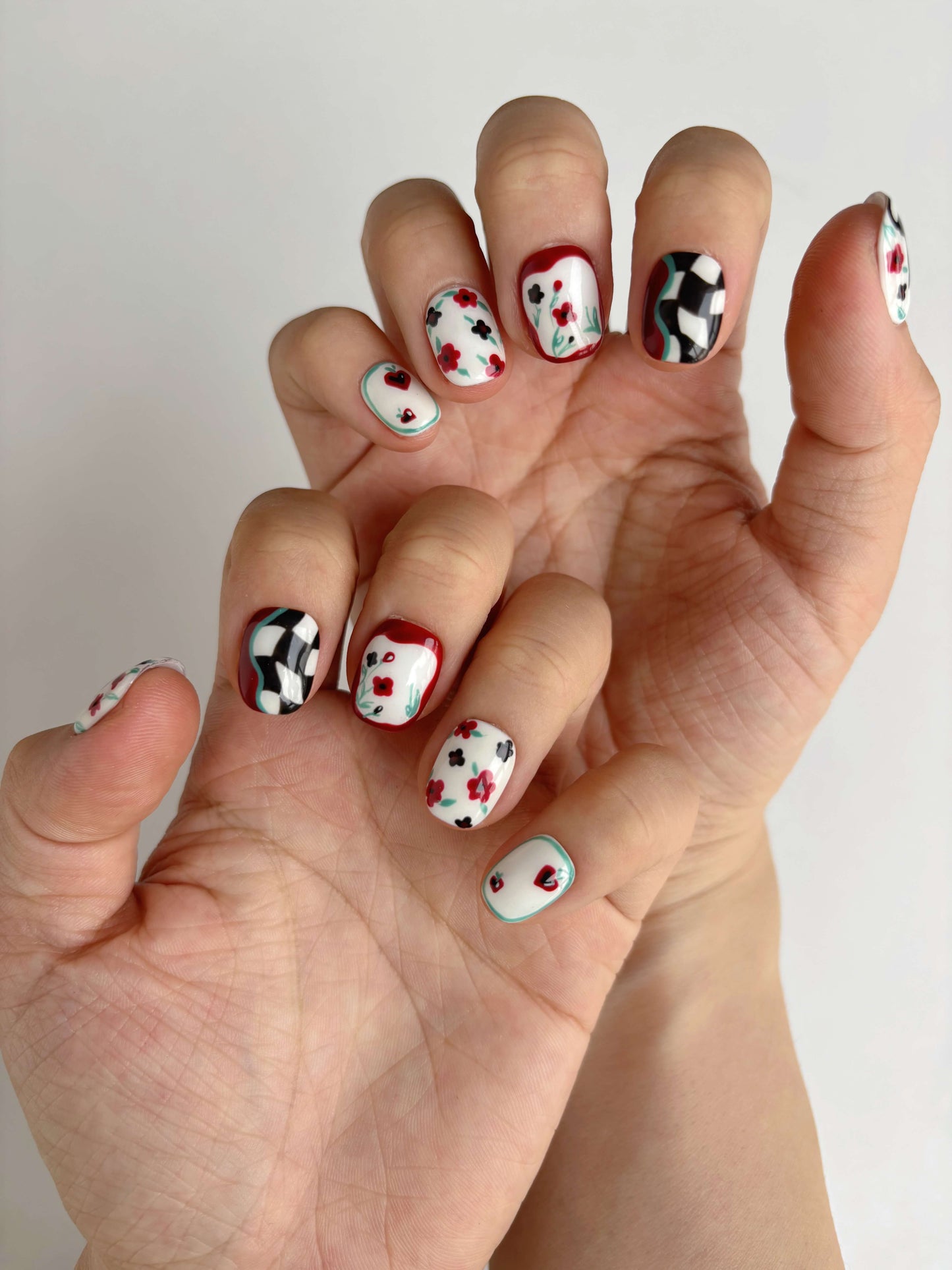 “Two hands showing full Lucky Cat Bloom press-on nail set with heart and wave patterns
