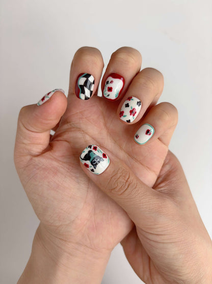 Hand wearing Lucky Cat Bloom nails with kawaii black cat and red flower accents